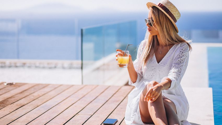 Giovane donna che beve un succo in piscina durante la sua esperienza di turismo di lusso in Italia.