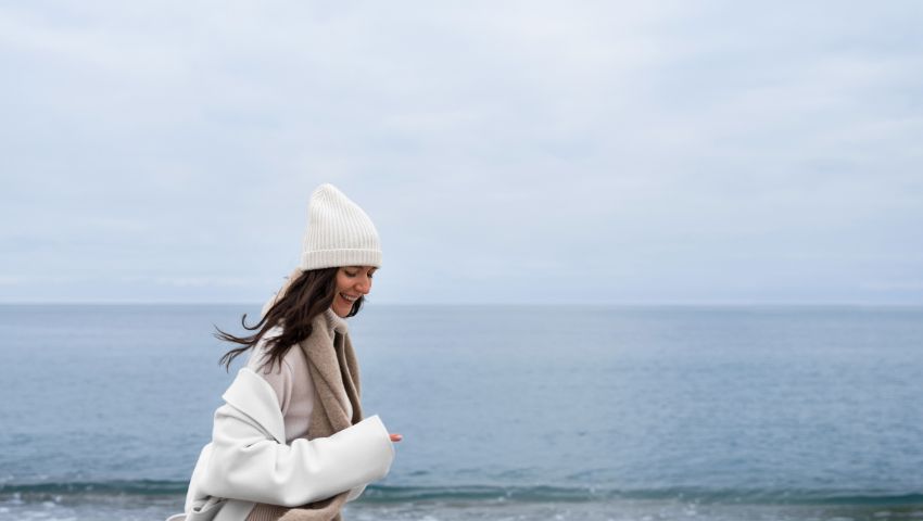 Donna sorridente in spiaggia d'inverno, a simboleggiar il turismo in bassa stagione.